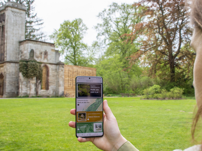App Weimar+ Frau hält Smartphone mit geöffneter Weimar+ App in Richtung Tempelherrenhaus