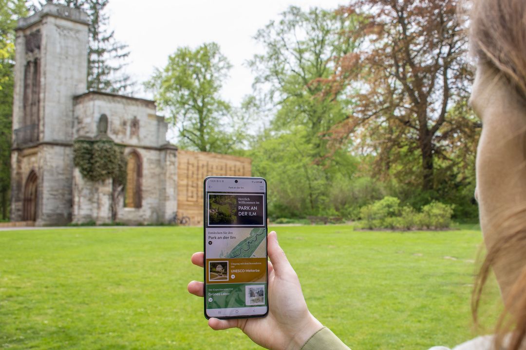 Weimar+ App Frau hält Smartphone mit geöffneter Weimar+ App in Richtung Tempelherrenhaus