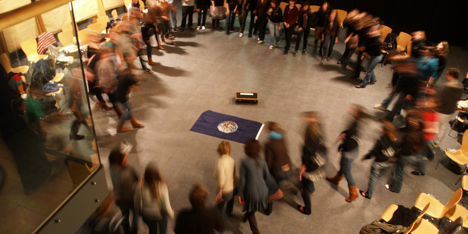 Persons arranged in a circle run towards each other, photographed from above