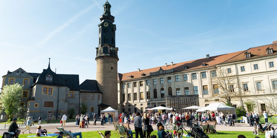 Stadtschloss Weimar bei der Themenjahr-Eröffnung 2025 Menschen sitzen und stehen auf einer grünen Wiese. Im Hintergrund ist ein großes Schloss.