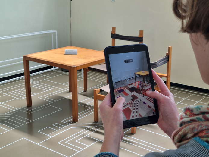 Mit der AR-Funktion in der App Weimar+ durch das Haus Am Horn Person mit Tablet blendet Rekonstruktion eines bunten Teppichs ein.