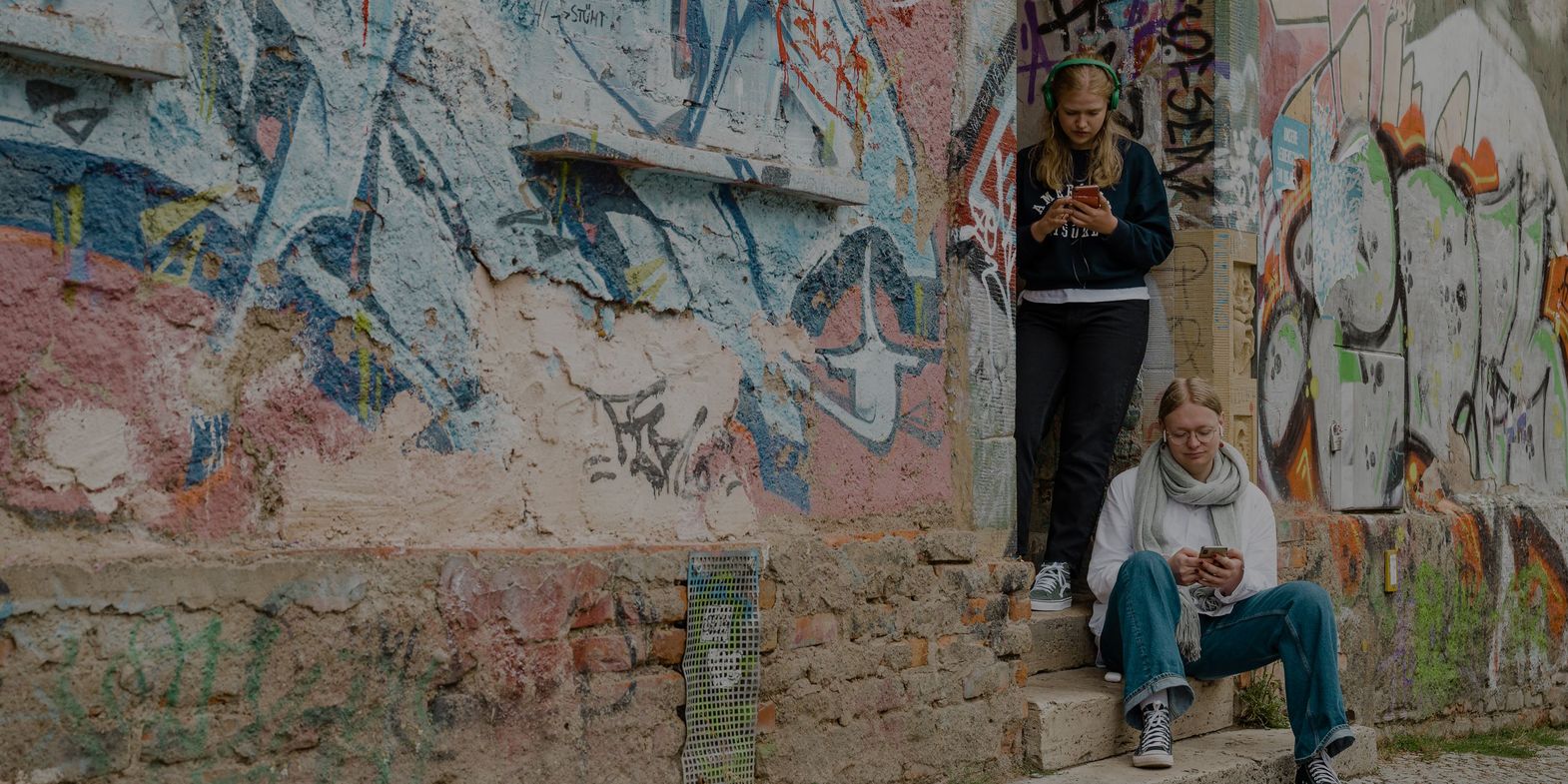 App Weimar+ Vor einer Hauswand mit viel Graffiti steht eine Gruppe von vier Personen, die gebannt auf ein Smartphone schauen und Inhalte der Kulturapp abspielen.