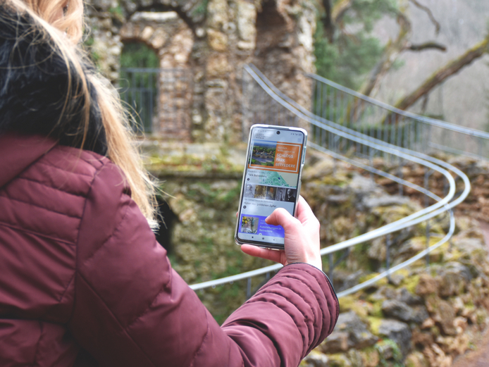 Mit der App unterwegs im Park Belvedere Frau hält ihr Smartphone mit geöffneter Weimar+ App im Park Belvedere