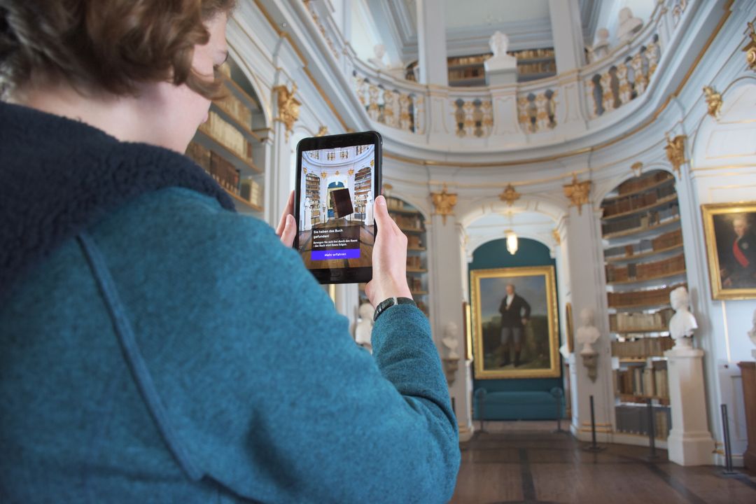 Mit der App Weimar+ im Rokokosaal Frau benutzt die Anwendung „Aufgeschlagen“ auf ihrem Smartphone im Rokokosaal.