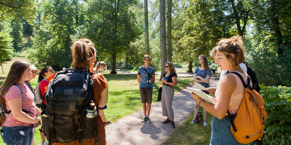 Gruppe junger Schüler*innen steht im Kreis aufgestellt im Park Tiefurt