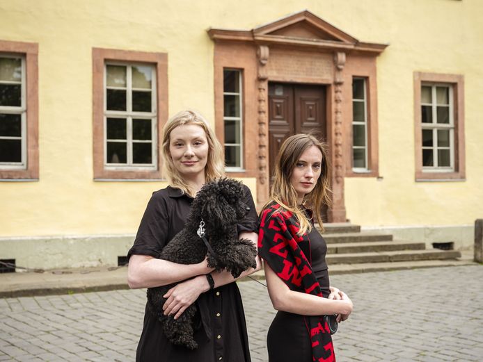 Podcast "Faust Forward" Zwei Personen mit einem schwarzen Pudel vor einem gelben Haus