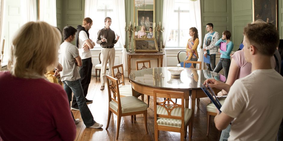 Gruppe steht mit Guide um runden Tisch in grünem Zimmer