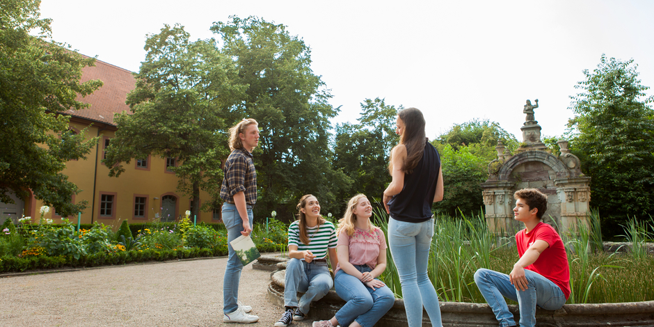 Fünf Jugendliche treffen sich an einem Brunnen vor dem Wielandgut